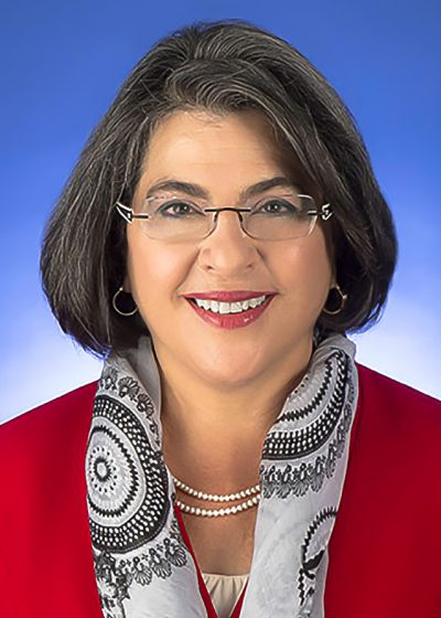 Daniella in a red top and grey scarf over a blue background