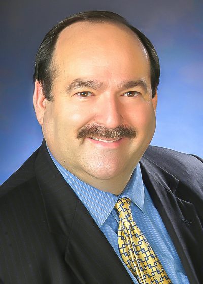 Steve in a dark jacket, blue shirt, yellow tie over a blue background